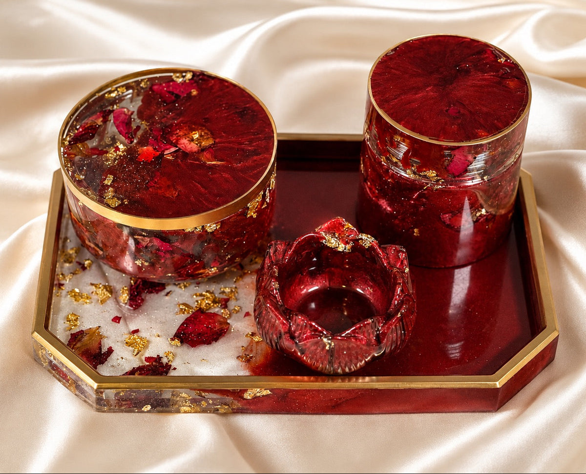 Three red resin decorative containers with gold trim and dried flower inclusions, displayed on a matching red and gold tray over a cream satin fabric background.