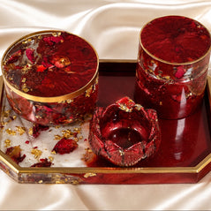 Three red resin decorative containers with gold trim and dried flower inclusions, displayed on a matching red and gold tray over a cream satin fabric background.