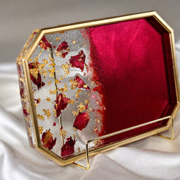 An octagonal decorative tray with a gold metal frame, featuring a split design of deep red velvet on one side and a clear side filled with dried red rose petals and gold leaf flakes on the other. The tray is displayed on a white satin fabric background.