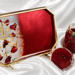A decorative octagonal tray with a gold frame and a translucent red-and-white design, shown alongside a glass jar and lid containing a red preserve or jam, all arranged on white satin fabric.